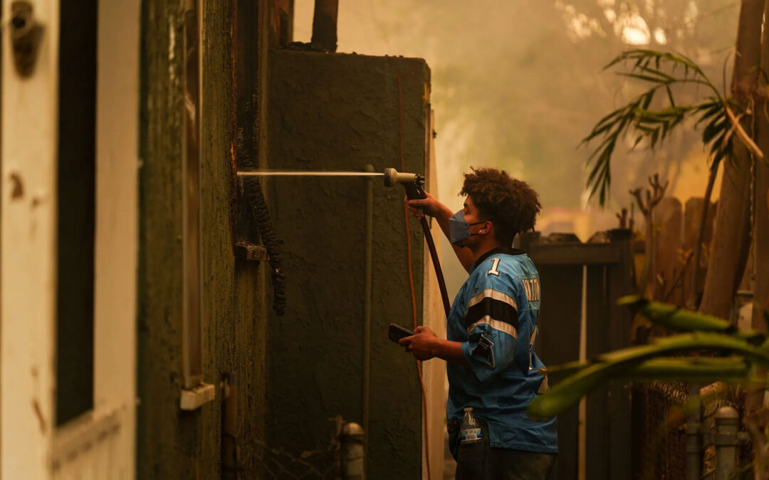 A person uses a hose to spray water on the flames of a house to prevent the Eaton Fire from spreading to other homes in an Altadena neighborhood on Jan. 8, 2025. Photo by Jules Hotz for CalMatters