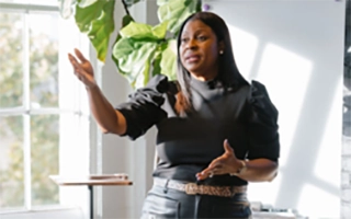 Tunua Thrash-Ntuk speaking in a room close to a window with the bright light from the sun shining in