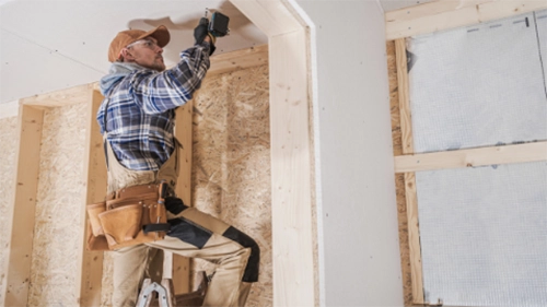 Construction worker standing on a ladder putting in drywall