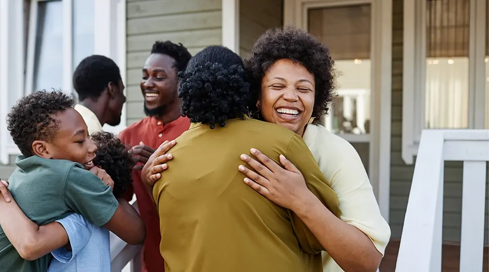 Happy family hugging and smiling seeing each other in front of their home
