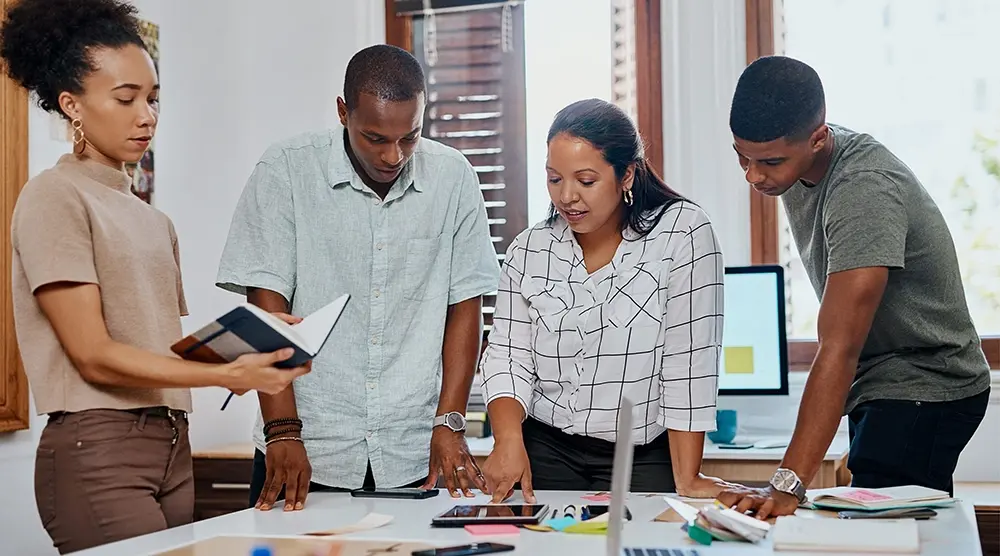 Group of four brainstorming over a table covered with miscellaneous items