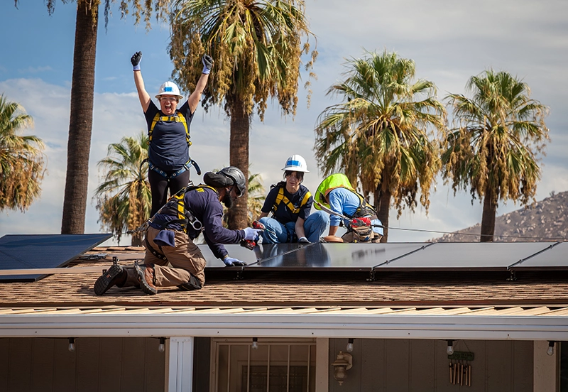Group of workers installing solar panels to a home with one worker standing and cheering