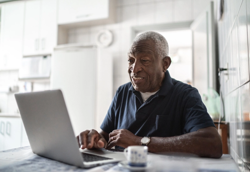 Elderly man browsing on his laptop sitting in the kitchen