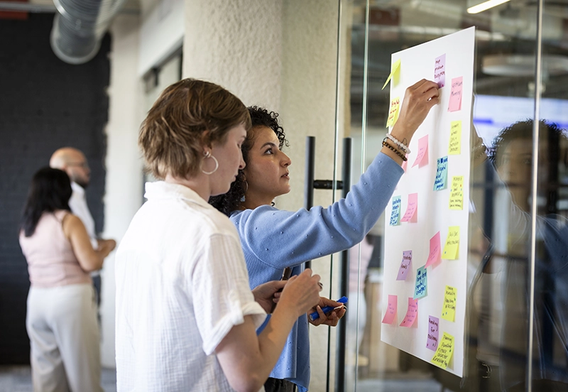 Two female employees strategizing on a white board using colored sticky notes