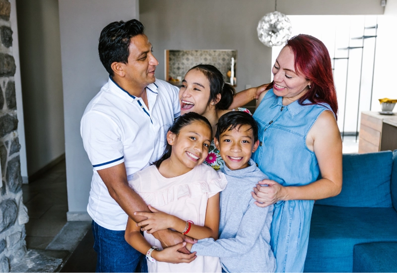 Happy family of five smiling and hugging in the middle of living room
